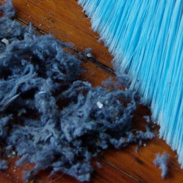 A broom with blue bristles, sweeping up a huge pile of lint.