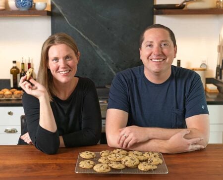 Adam and Joanne at the kitchen counter eating cookies, smiling at the camera.