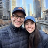 Kayla and Chris posing for a photo in front of a river and skyscrapers.