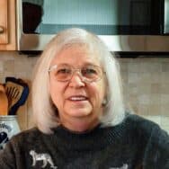 a woman with shoulder-length gray hair and glasses smiles at the camera
