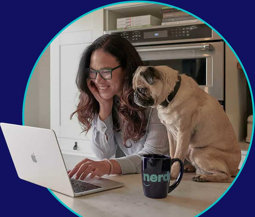 Melissa and her pug Kingston in the kitchen, looking at her laptop and smiling.