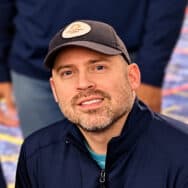 Felipe in a navy zip-up jacket and a dark baseball cap, smiling at the camera.