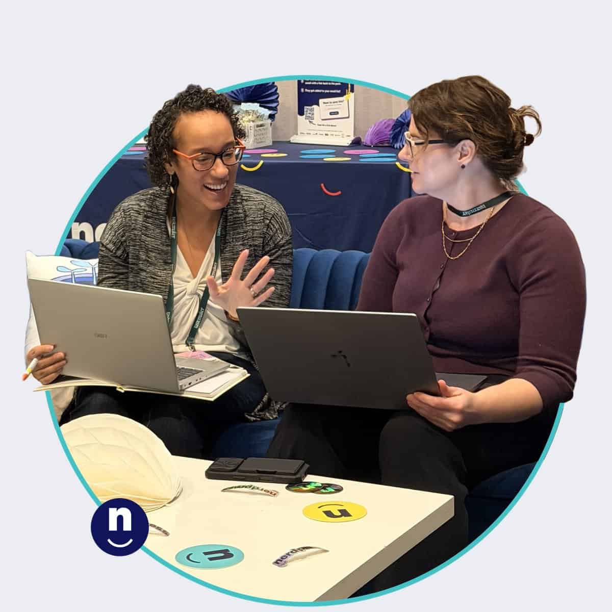 A NerdPress team member and a conference attendee sit side by side on a couch with laptops open, working through questions about the attendee’s website. The attendee is laughing and gesturing as she explains something while the NerdPress team member listens.